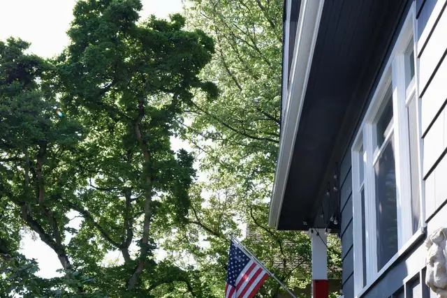 Blue two-story house with a covered porch, garden beds and a flag