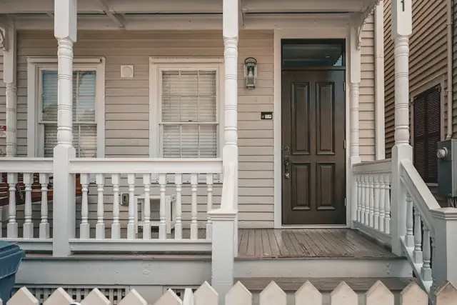 Classic wooden front porch with white railings, columns and a picket fence