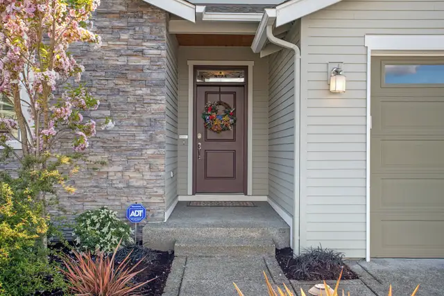 Front door of a gray house with stone siding and spring flowers