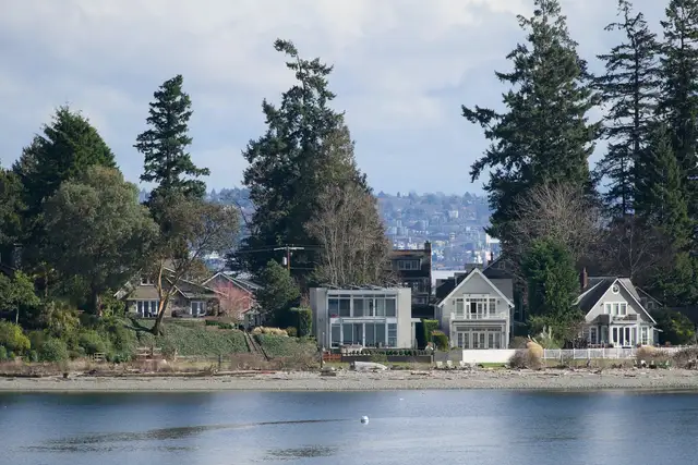 Waterfront homes among tall evergreens reflected in calm water