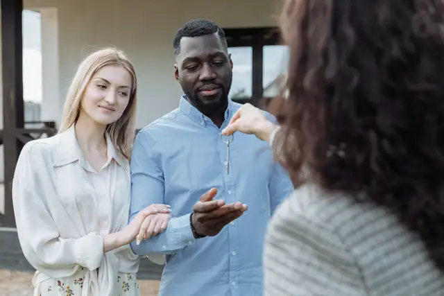 Agent handing a set of house keys to a young couple standing outside their new home