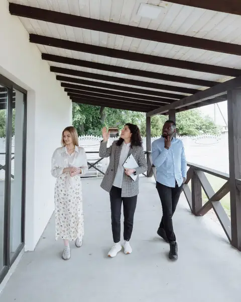An agent leading two clients along a covered porch during a home tour