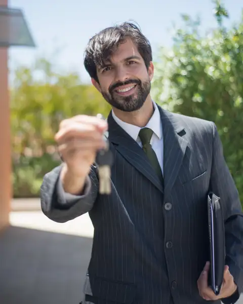 Reid Halvorsen outdoors in a dark suit, smiling and holding up a house key