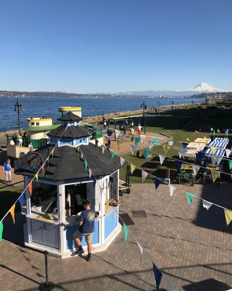 Waterfront promenade with a small kiosk, flags and Mount Rainier in the distance